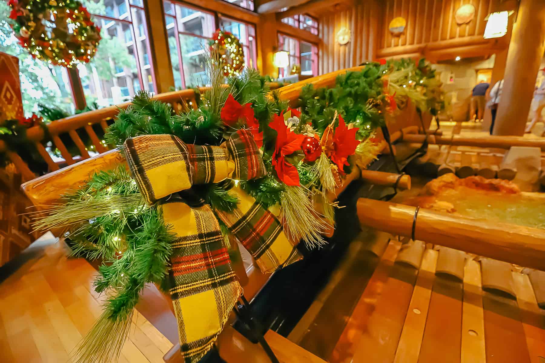 Garland with a large plaid bow tied to the bridge that runs over Copper Creek in the Wilderness Lodge's lobby.