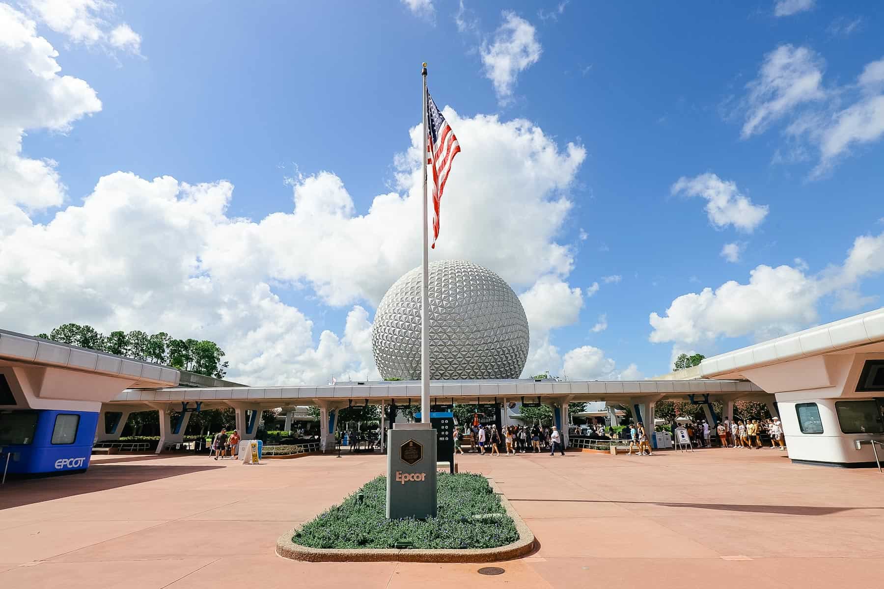 Epcot's entrance from the parking lot with the American flag and Spaceship Earth in the background. 