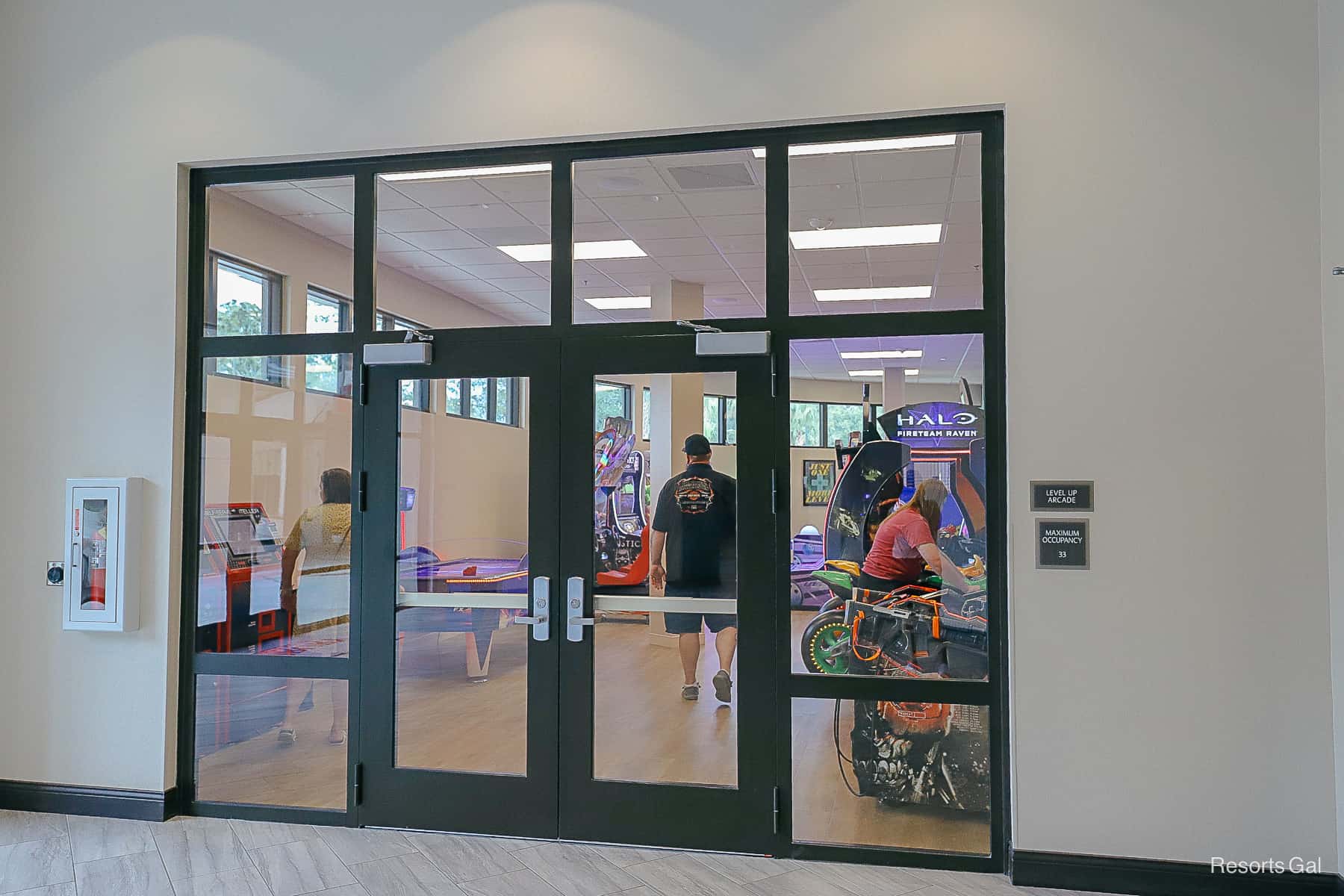 A pair of glass doors opens up to a busy arcade with people playing games. 