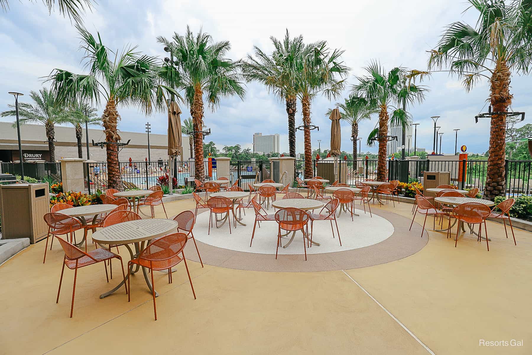 Outdoor tables and chairs on a patio surrounded by palm trees. 