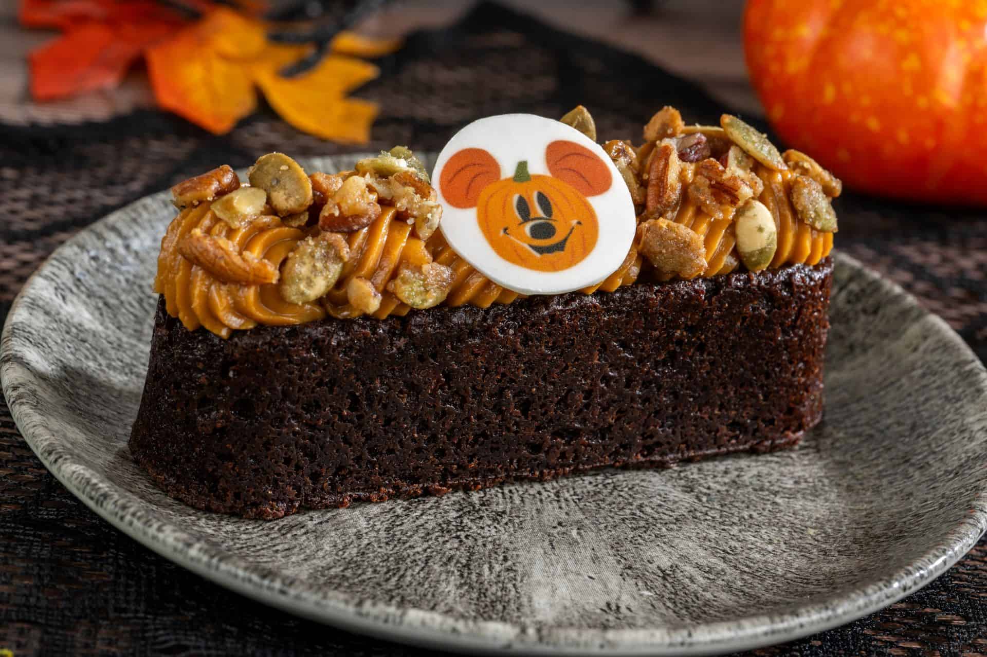 a brownie bar topped with icing, nuts and a pumpkin Mickey Mouse