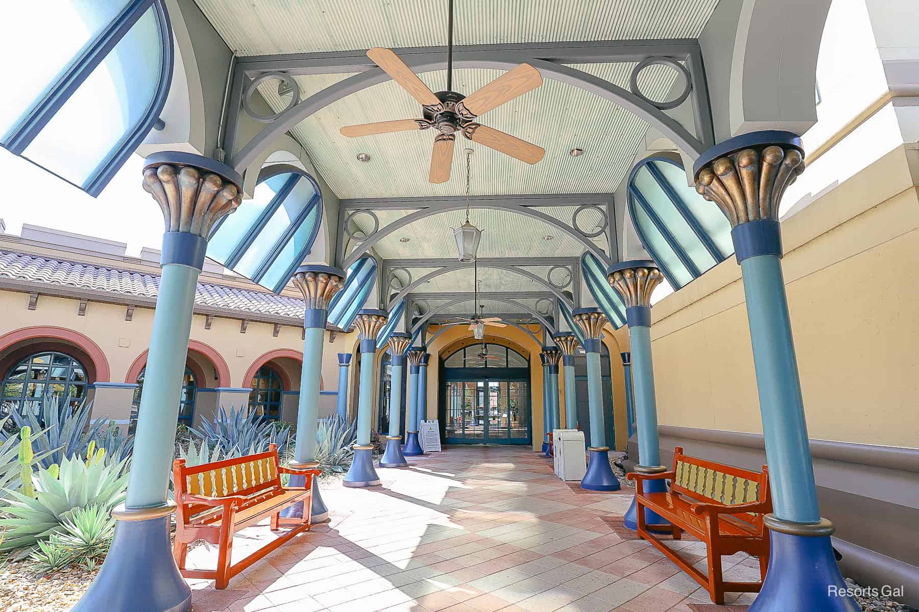 a long walkway with tile flooring, painted shades of blue and golds with large ceiling fans overhead