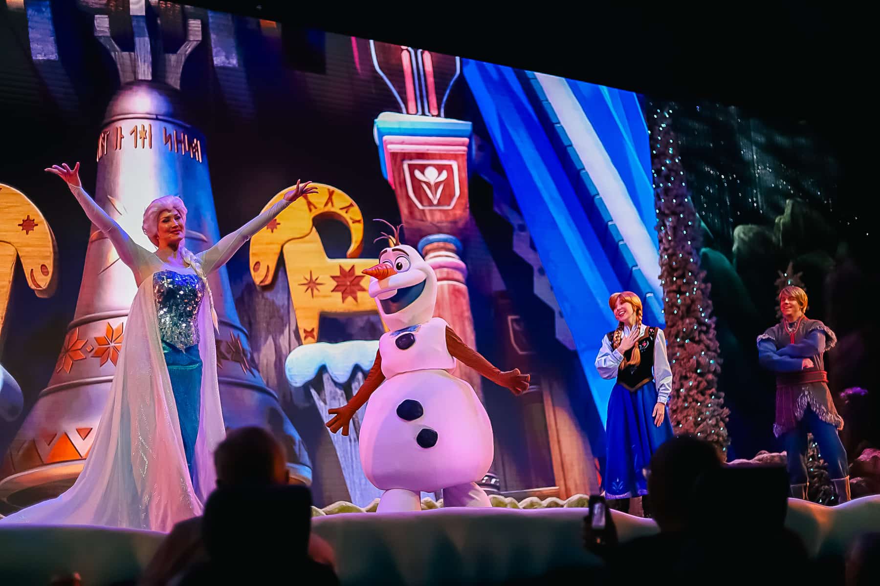 Elsa on stage with Olaf while Anna and Kristoff look on from the background. 