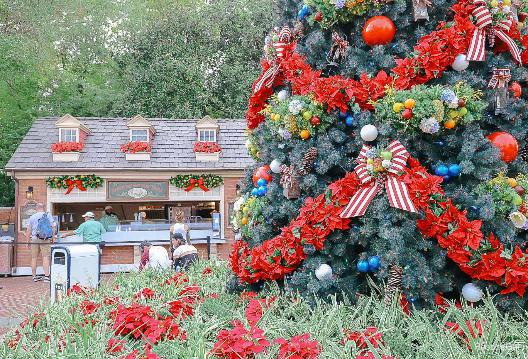 a holiday kitchen sitting behind a giant outdoor Christmas tree trimmed in red, white, and blue at Epcot during the Festival of the Holidays