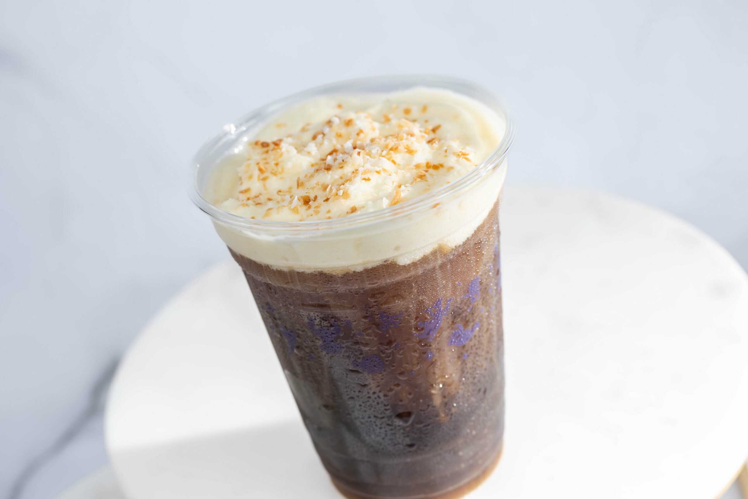 a cold brew coffee in a clear plastic cup topped with foam and toasted coconut