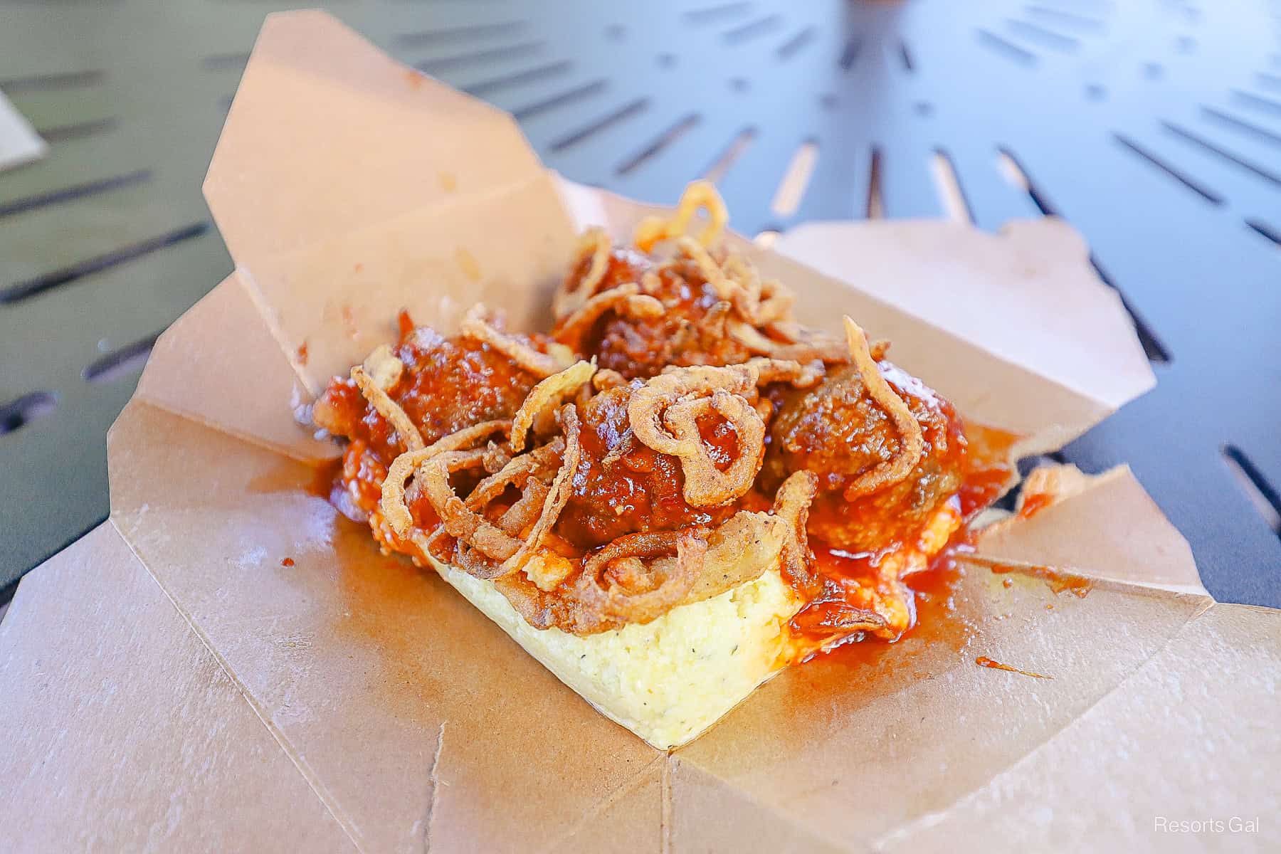 the sides of the to-go container folded down to reveal the polenta underneath the meatballs 