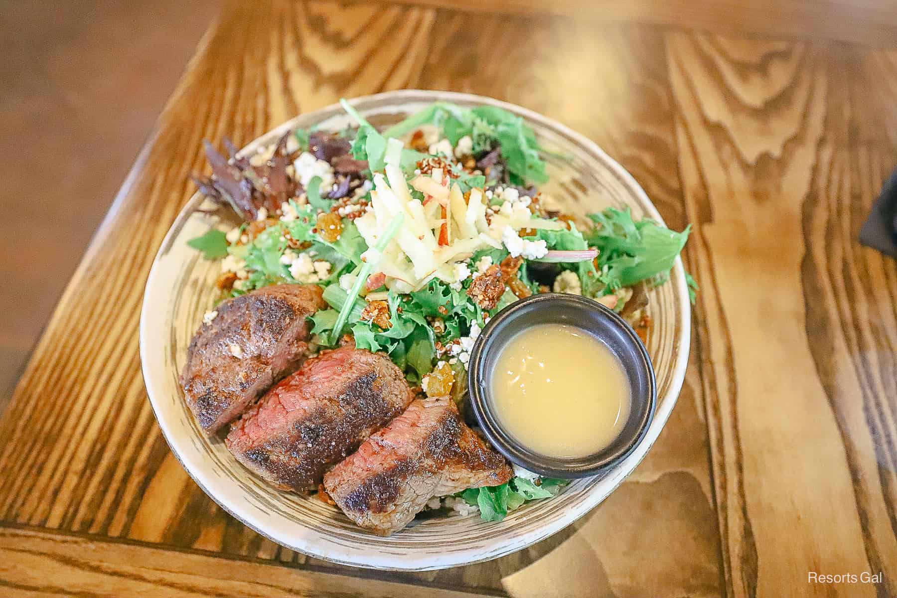 a steak salad with toppings and a side of vinaigrette 