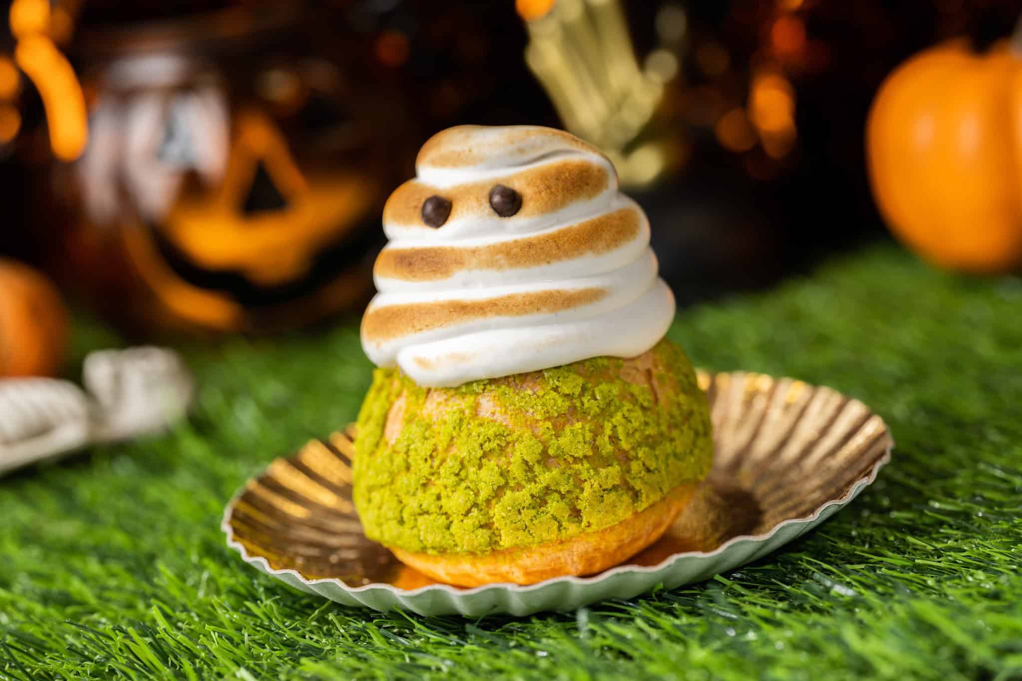 a cream puff topped with meringue that looks like a ghost with chocolate eyes 