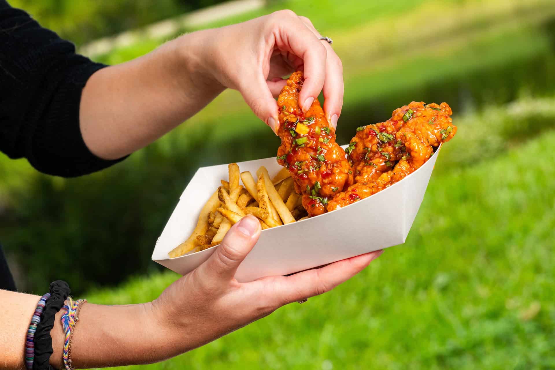 a hand holding a box with chicken fingers and fries