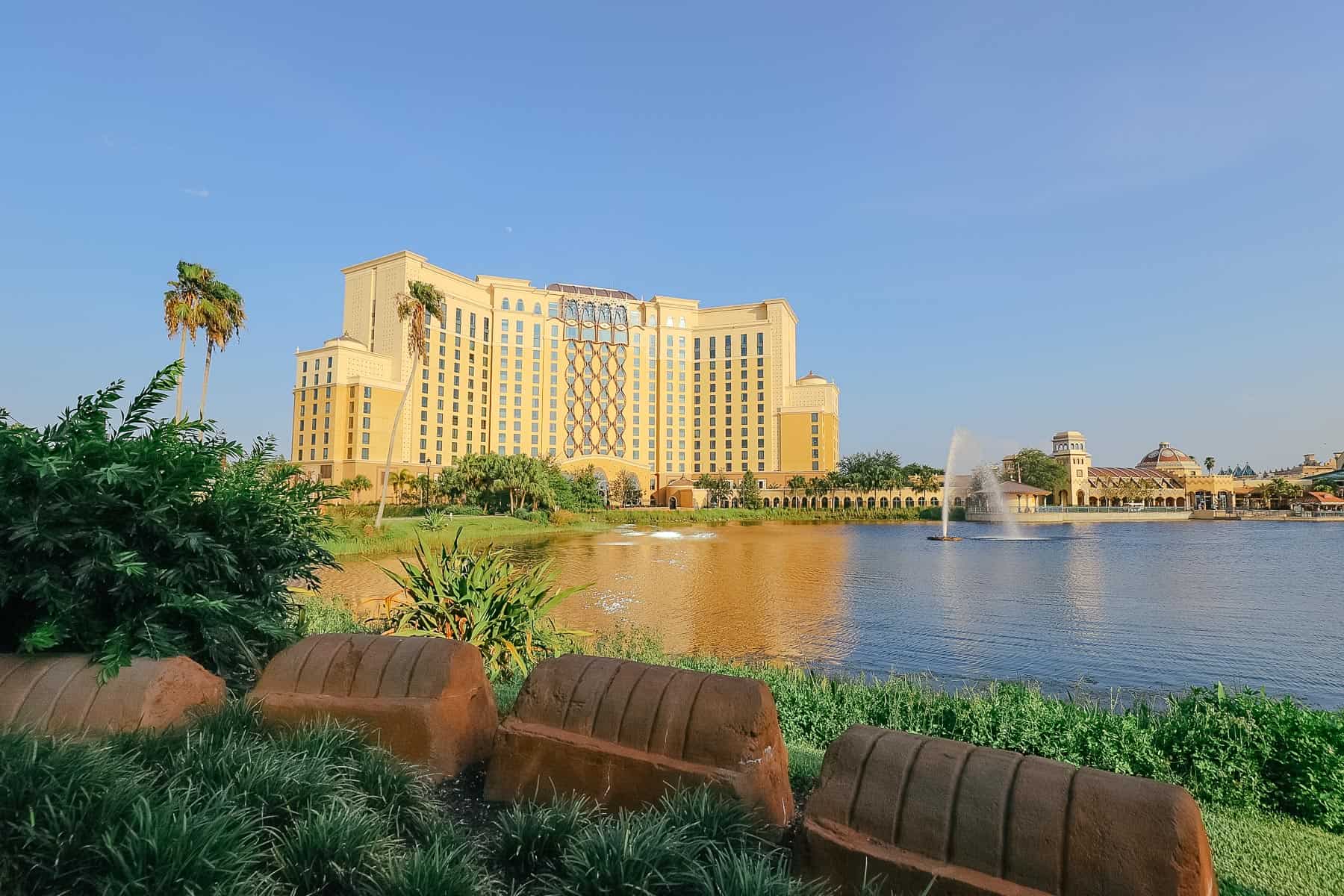 a view of Gran Destino Tower with the sun shining on it and the water fountain in the lake in front of it 