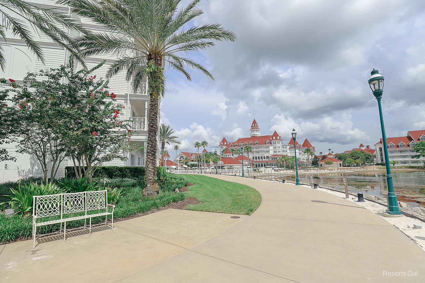 a bench with palm trees and light poles along the walking path