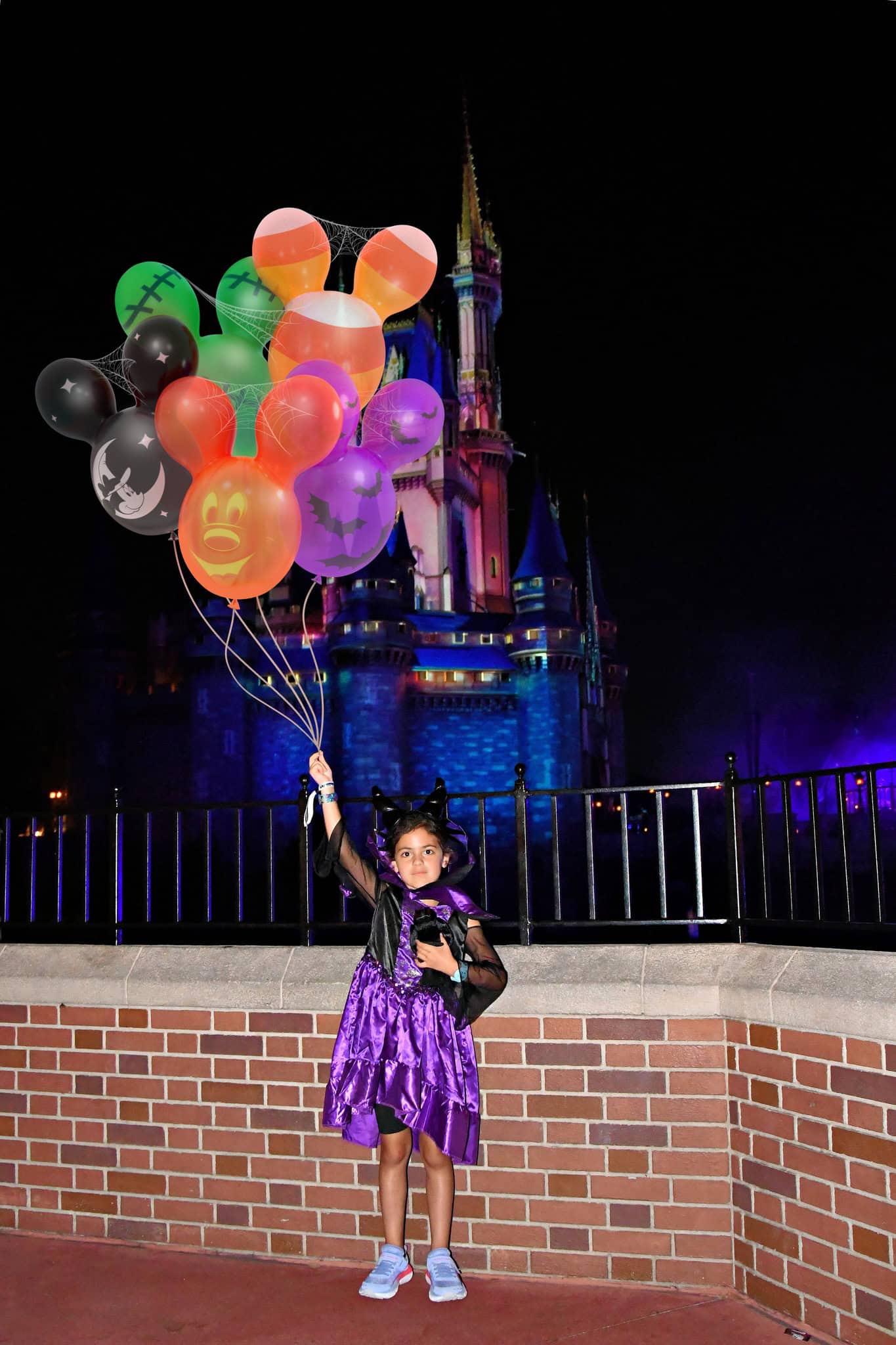 a guest holding a bouquet of balloons with Halloween designs in front of Cinderella Castle 