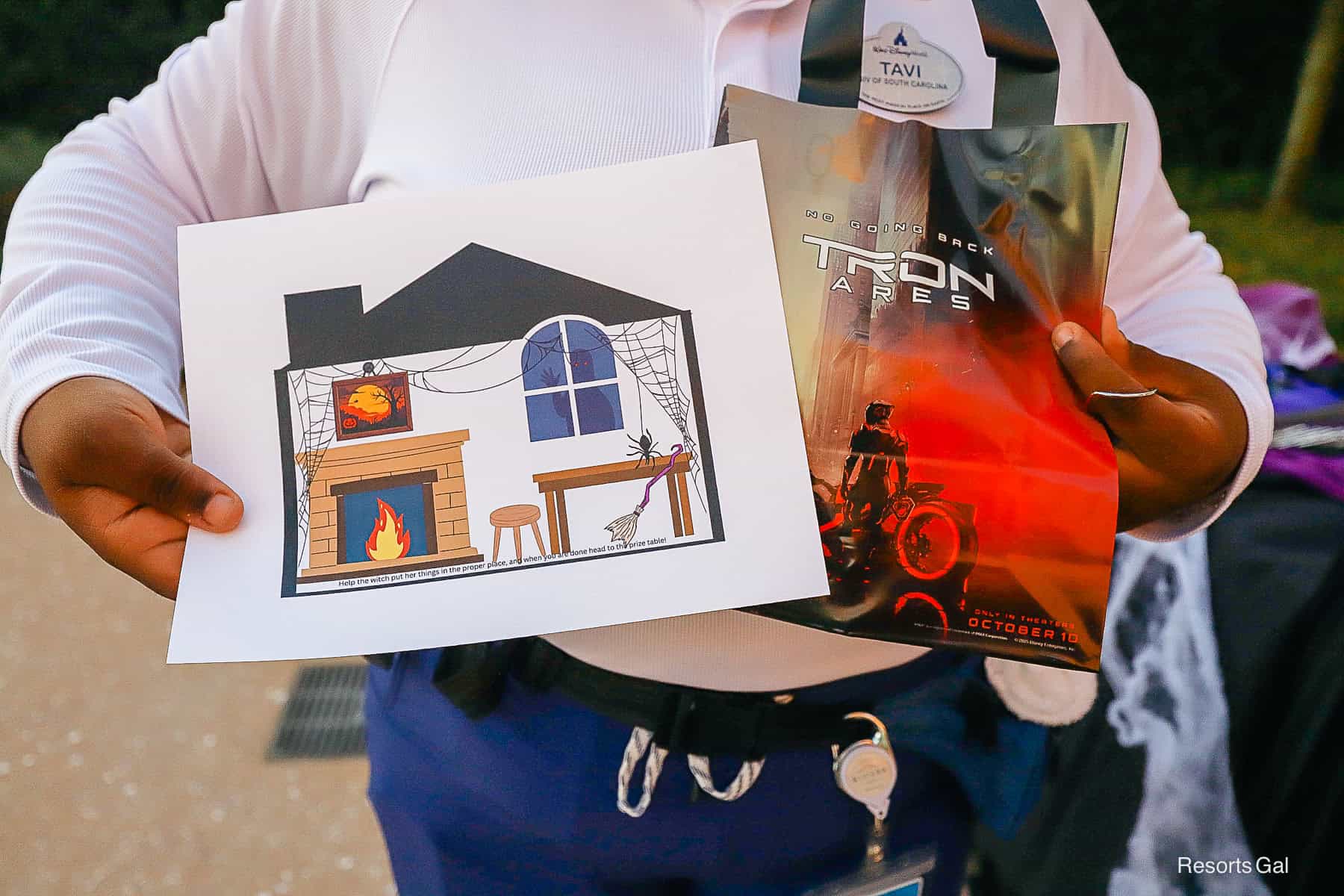 a cast member holds an activity sheet and a trick or treat bag for guests