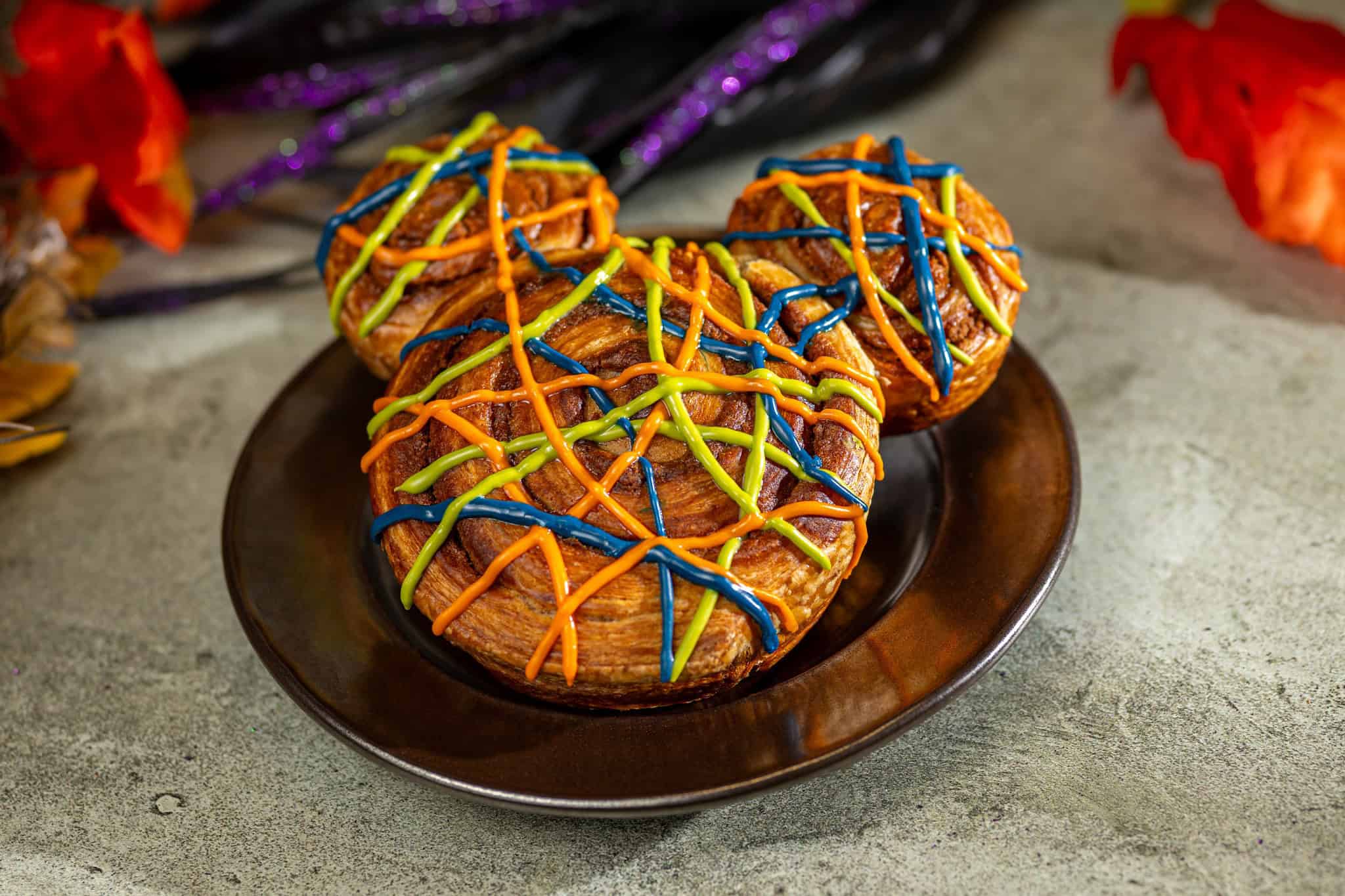 a mickey shaped cinnamon roll that's covered in purple, slime green, and orange drizzle 