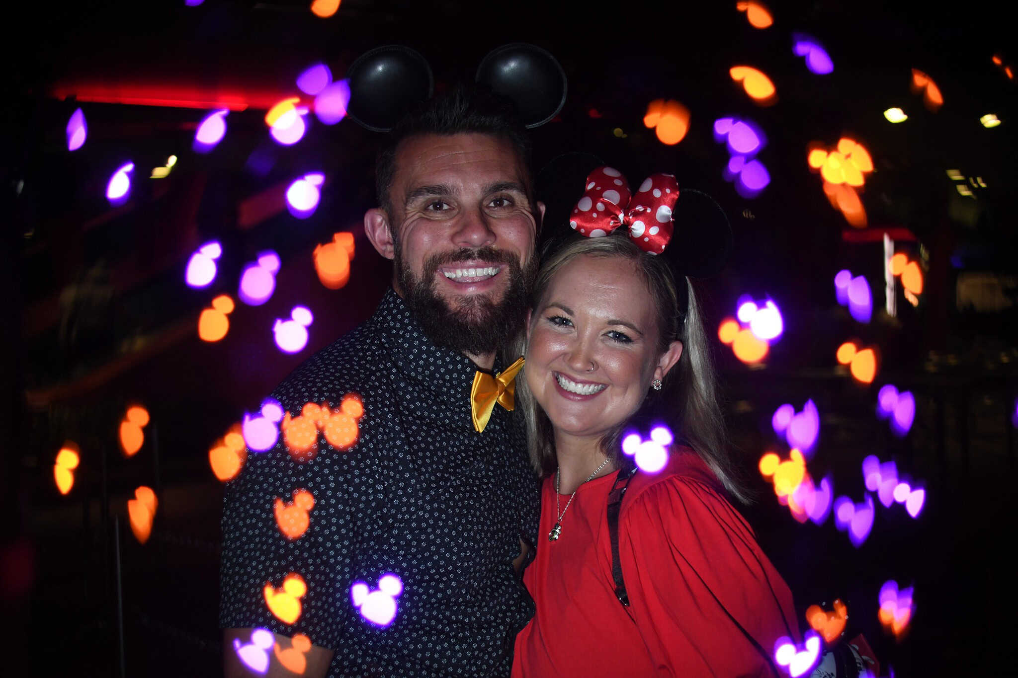 a couple taking a Halloween Photo at the party surrounded by glowing Mickey's in purple and orange 
