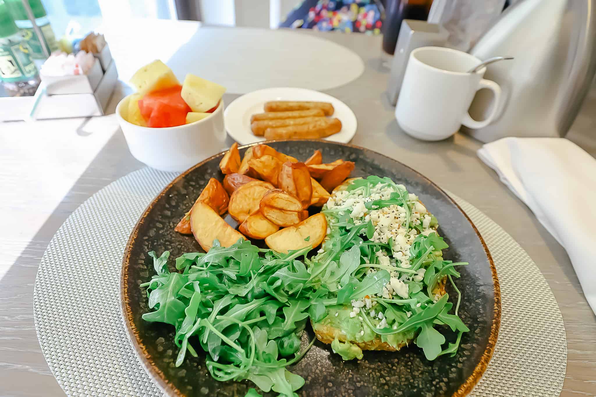 a plate with avocado toast, potatoes, sausage and fruit 