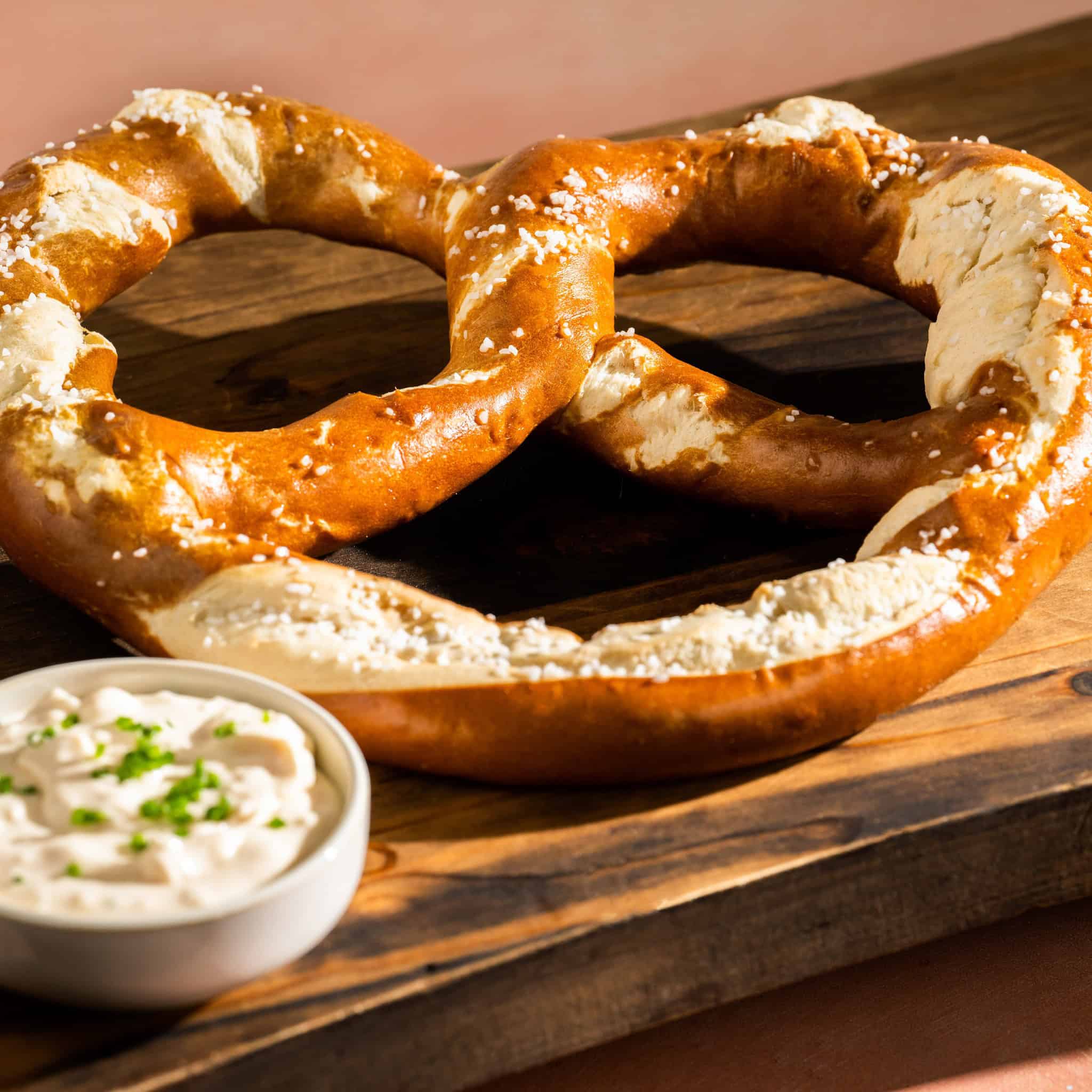 a giant pretzel on a wooden butcher block with cheese dip 