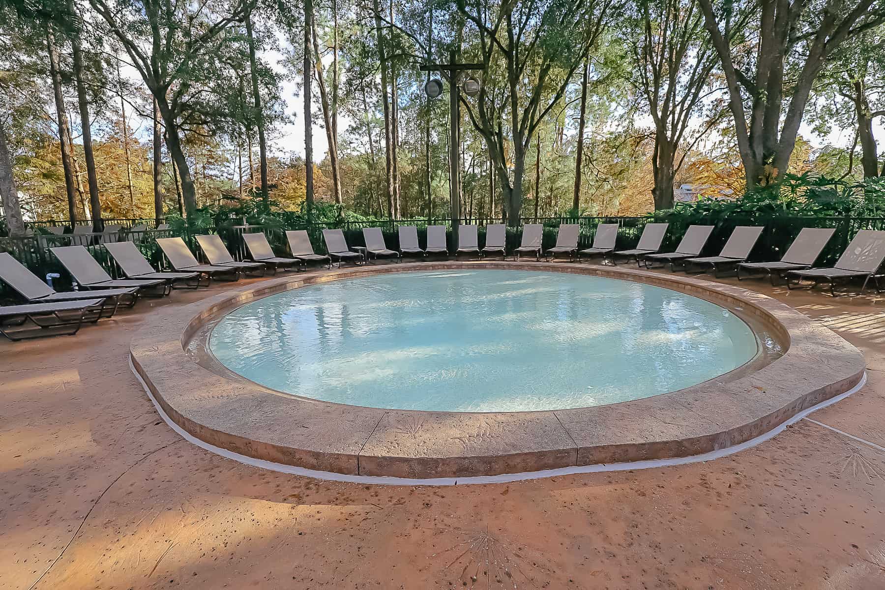 a kiddie pool sitting in the shade surrounded by lounge chairs 