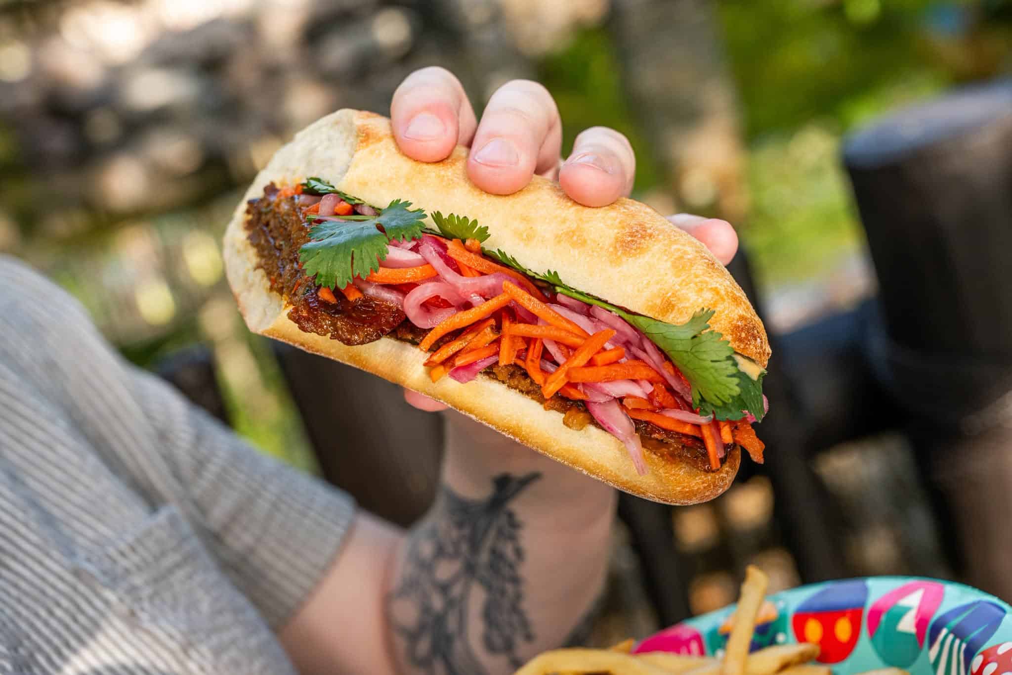 a hand holding a plant-based sandwich from Flame Tree Barbecue
