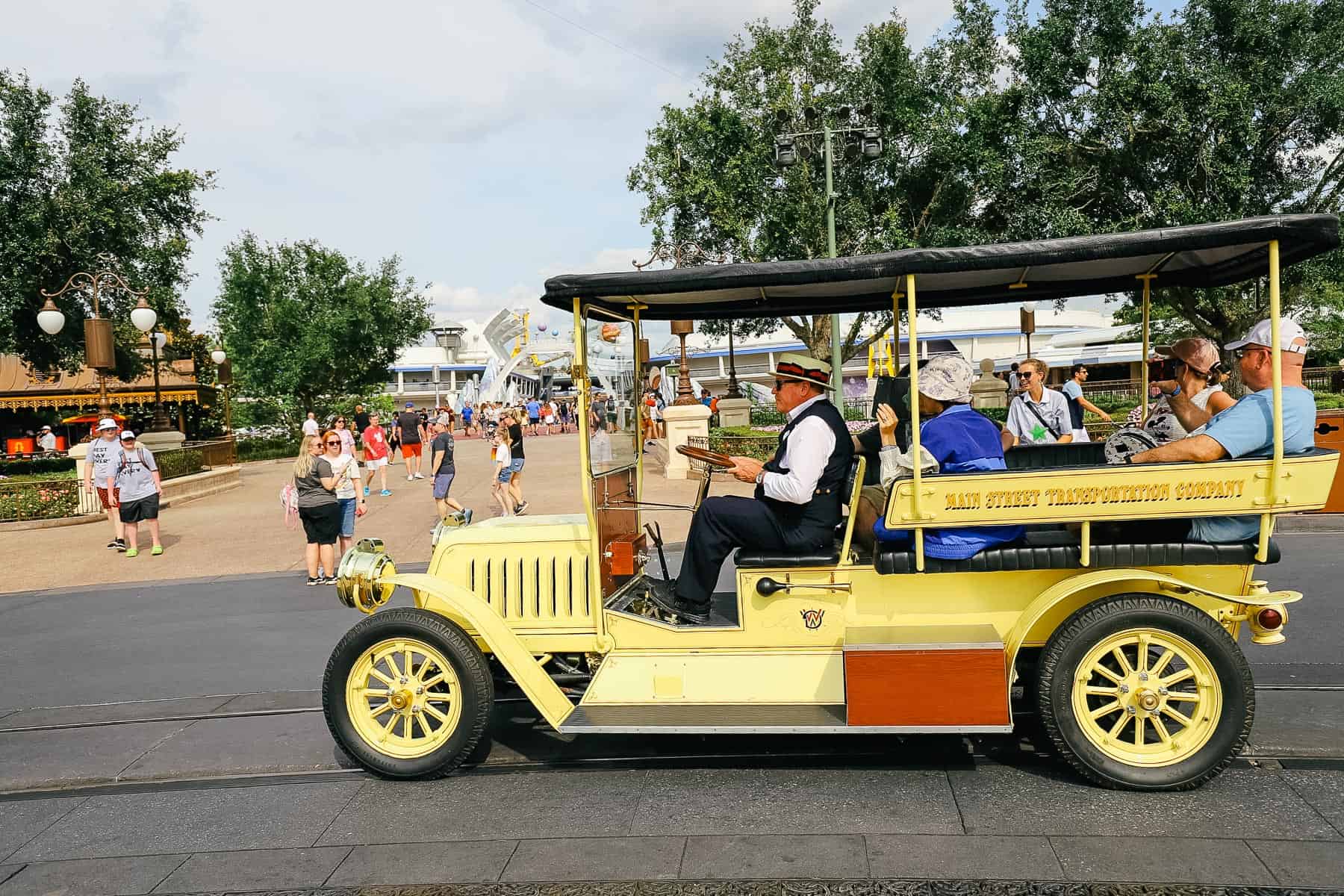 A cast member driving guests in a yellow Jitney around Cinderella Castle hub. 