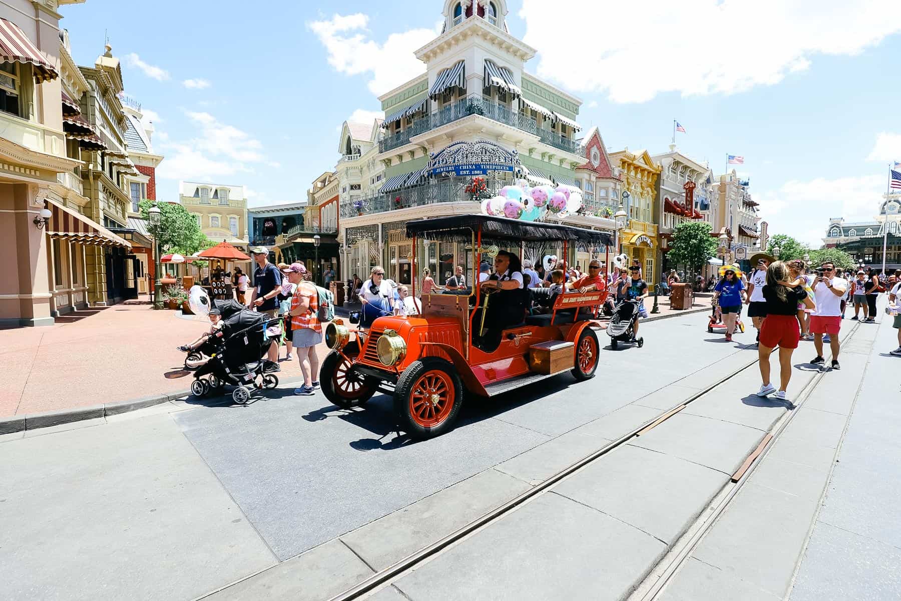 Guests riding through Magic Kingdom in a red Jitney. 