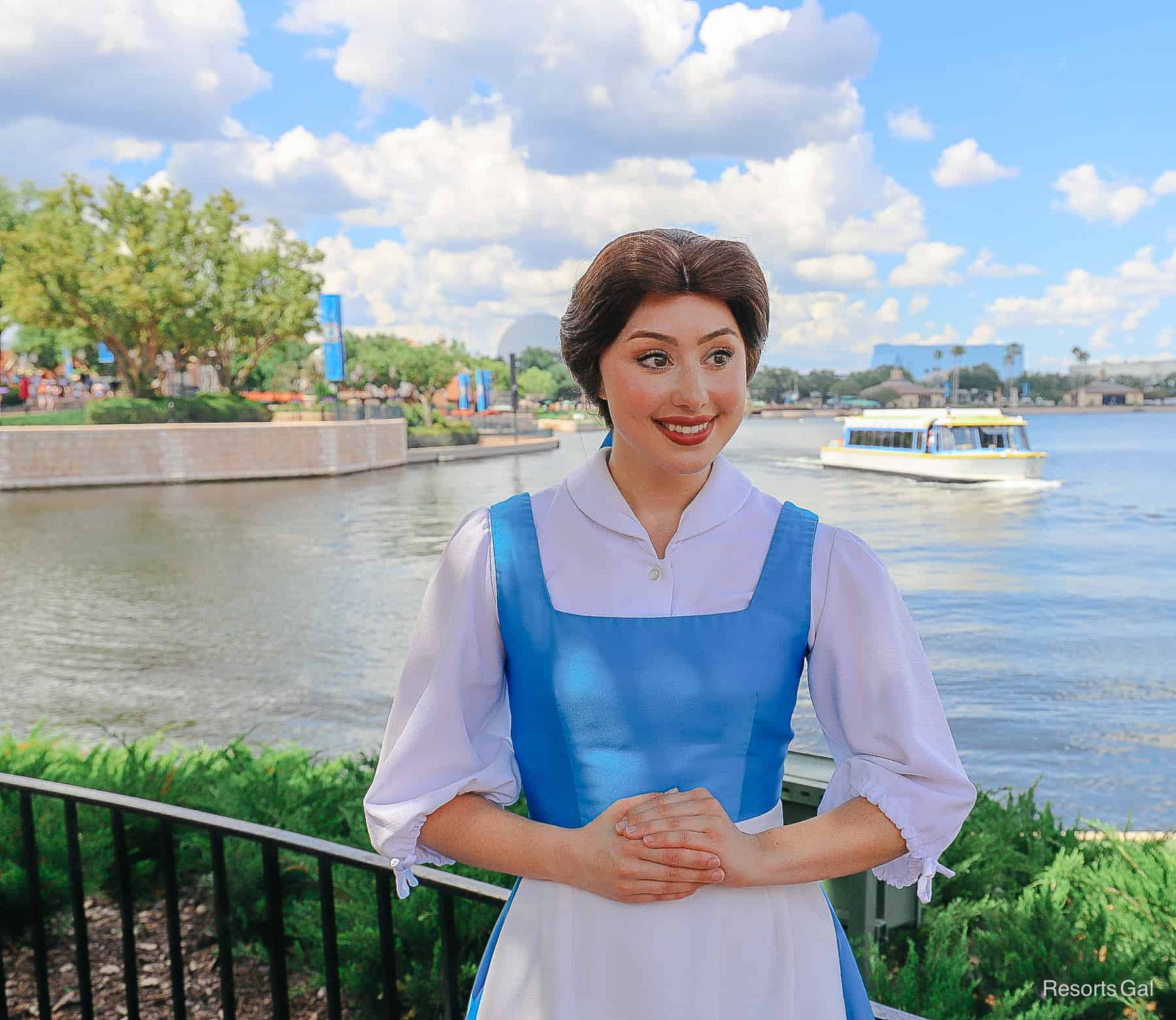 Belle poses for a photo with her hands clasped in front of her. She's wearing her blue village dress. 