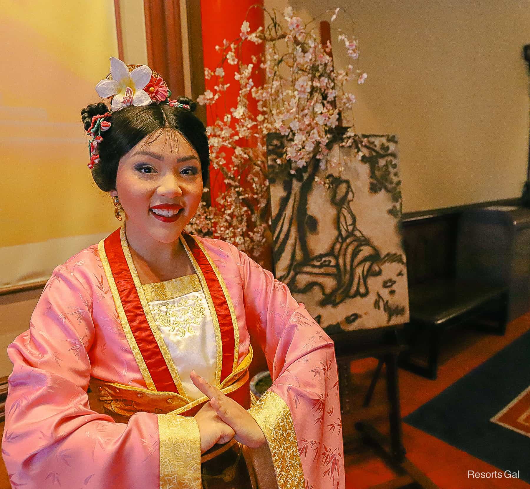 Mulan poses with her formal dress in pink with red and gold trim. 