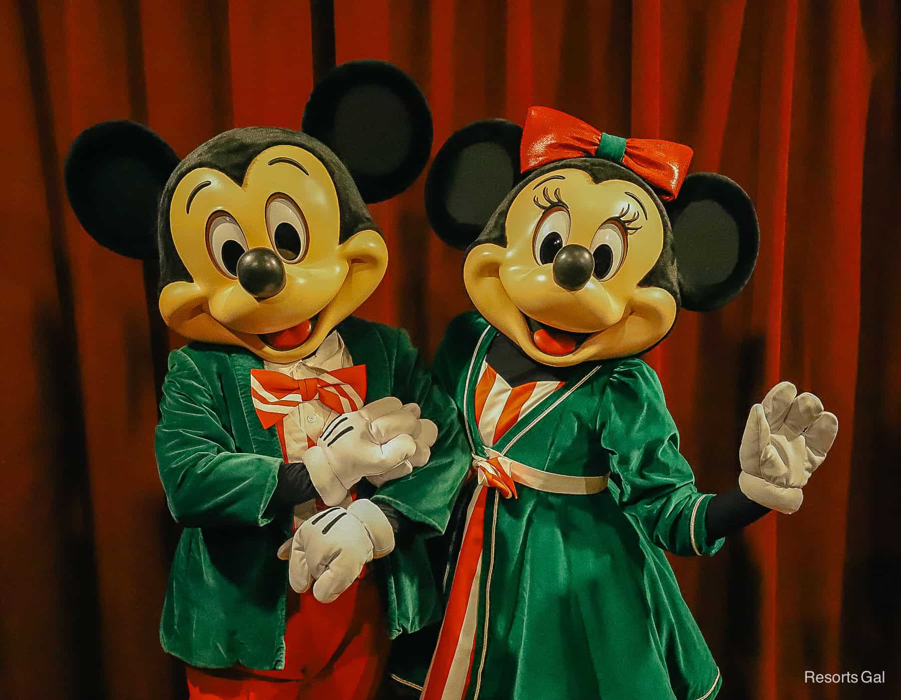 MIckey Mouse (L) wears a green velvet jacket with red bow tie and Minnie Mouse (R) wears a matching dress with red bow 