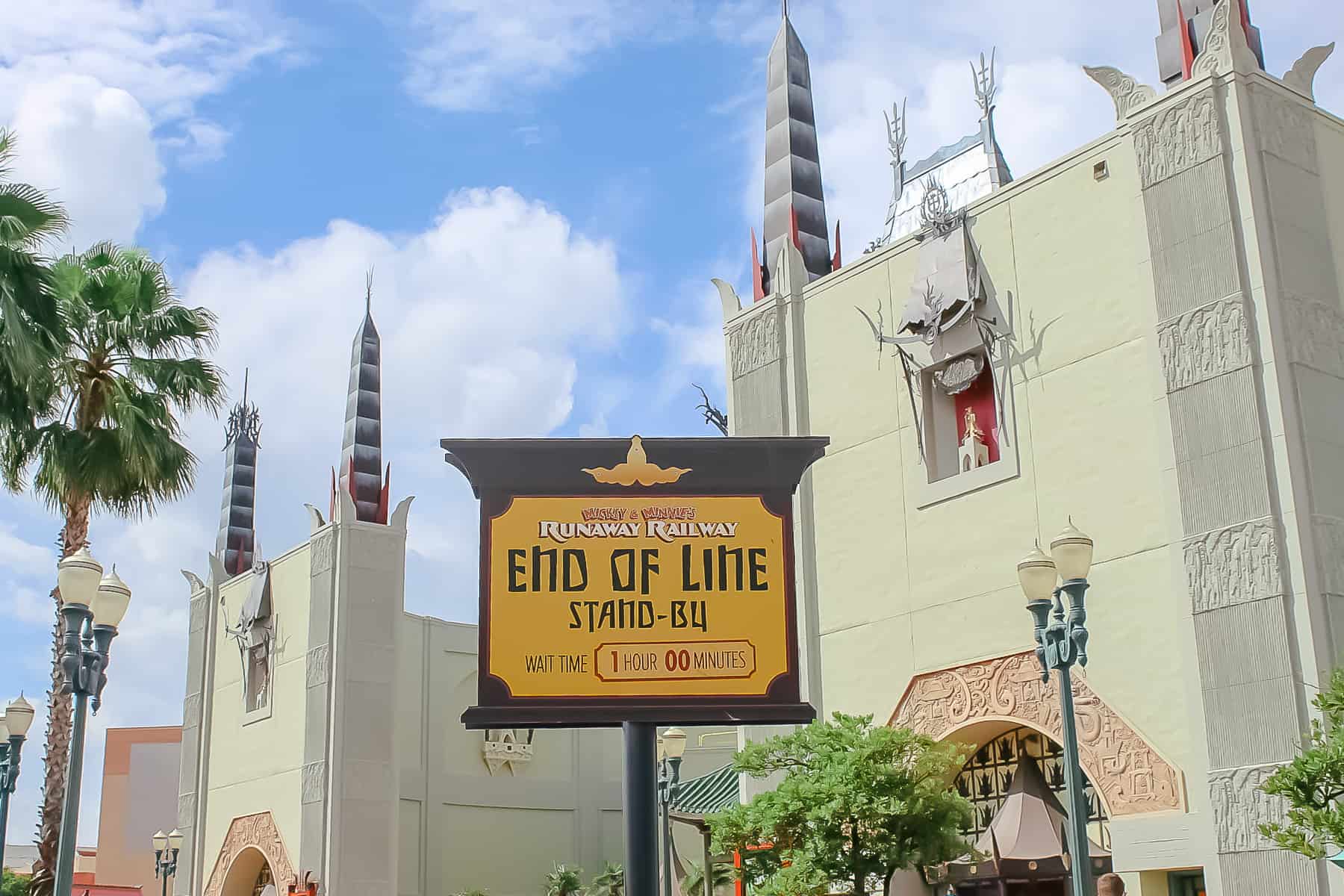 A cast member is holding up an end of the line sign for the stand-by queue. 