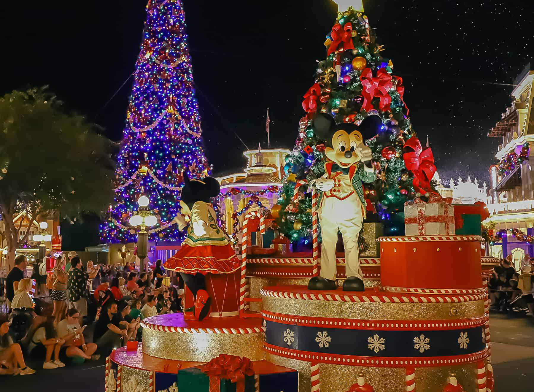 Mickey points to someone in the crowd during the parade with the Christmas tree in the background. 