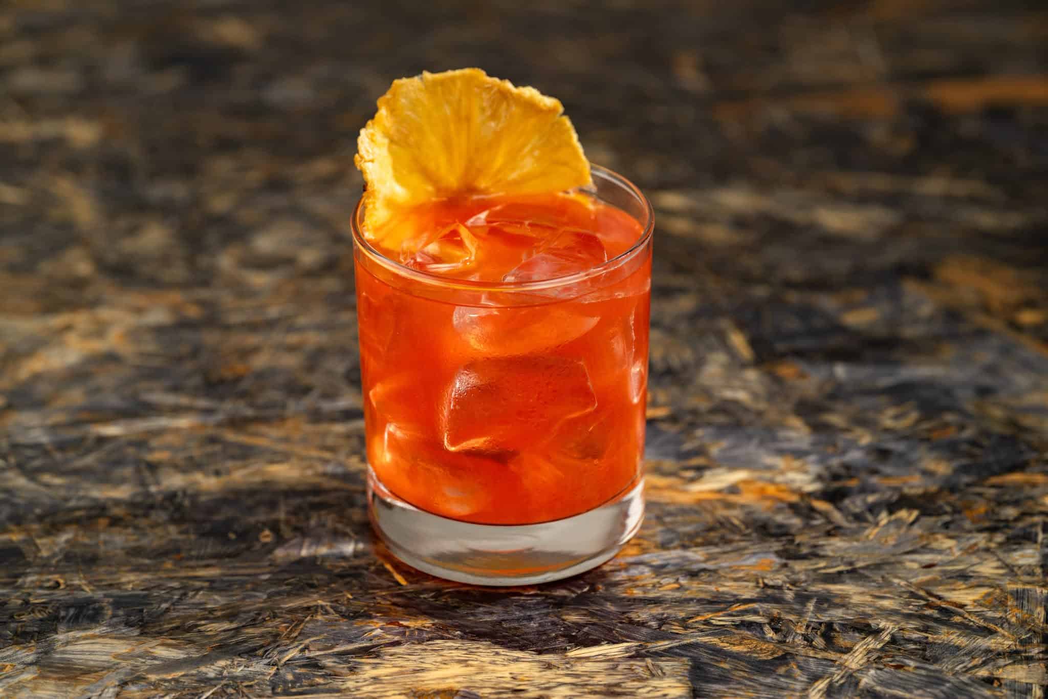 an orange cocktail poured over a glass of ice with a yellow accent
