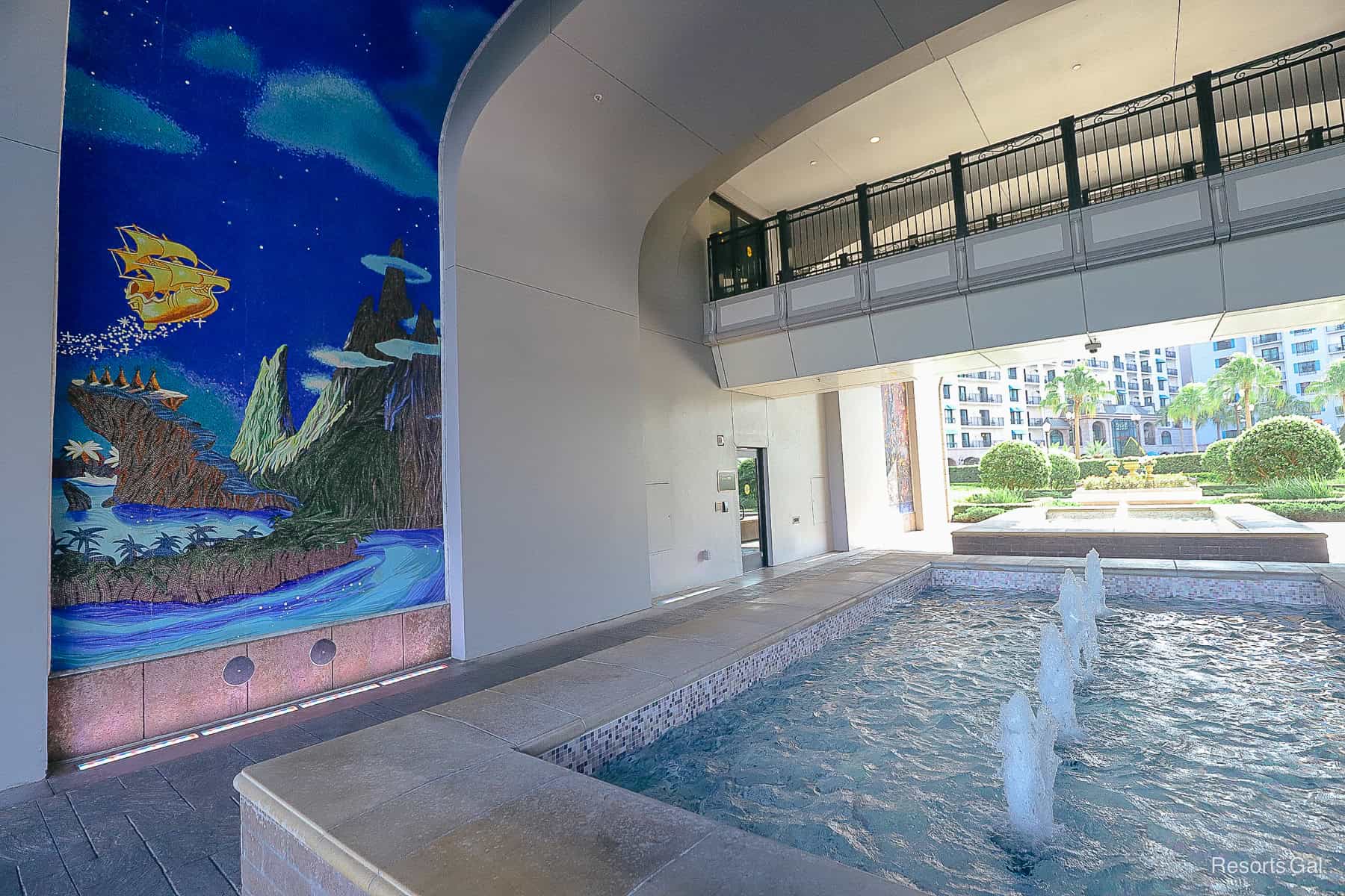 a mural next to a found and a bridge that connects hotel rooms overhead 