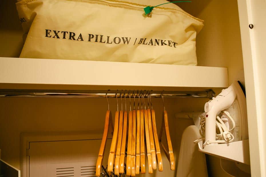 a closet with an iron, ironing board, extra pillow, and blanket 