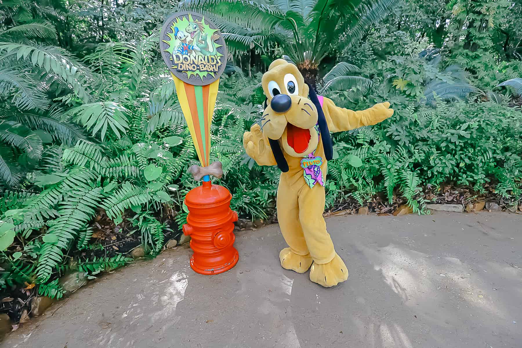 Pluto poses for a photo next to Donald's Dino-Bash sign 