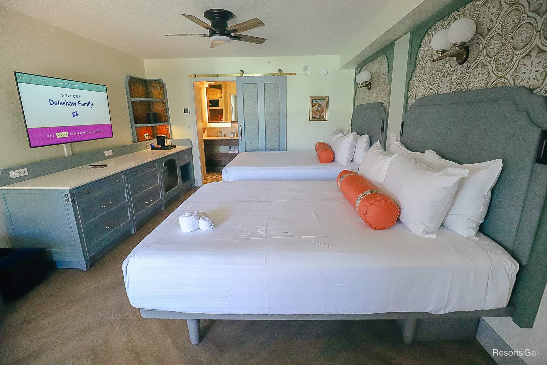a side angle of two queen beds with pillows and sage color headboards