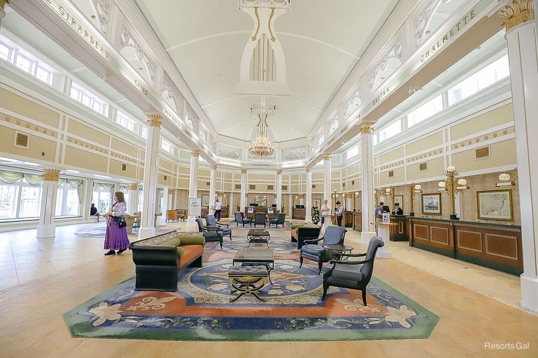 The interior lobby is tan with lots of white trim. It's a long lobby with traditional rugs and furniture. 