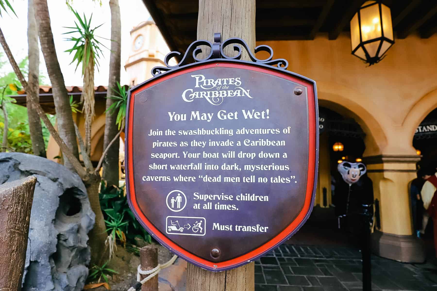 A sign that warns guests that they may get wet. It reads, "Join the swashbuckling adventures of pirates as they invade a Caribbean seaport. Your boat will drop down a short waterfall into dark, mysterious caverns where dead men tell no tales."