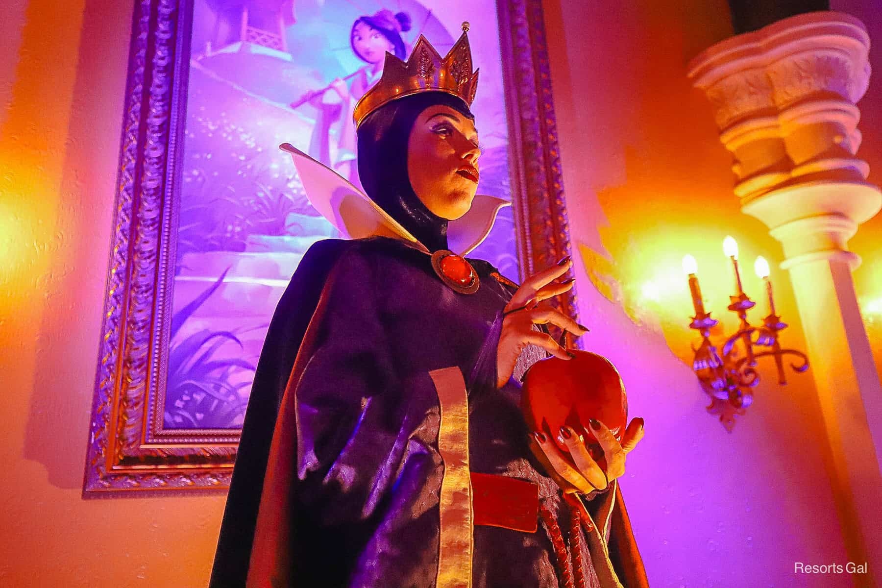 The Evil Queen holds an apple while posing for a photo in Princess Fairytale Hall.