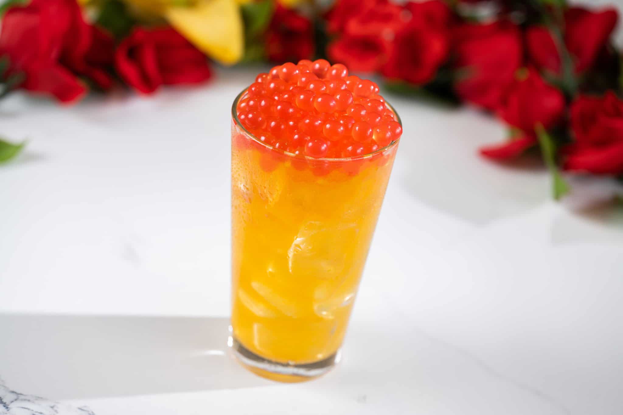 a drink that's yellow topped with red boba balls 