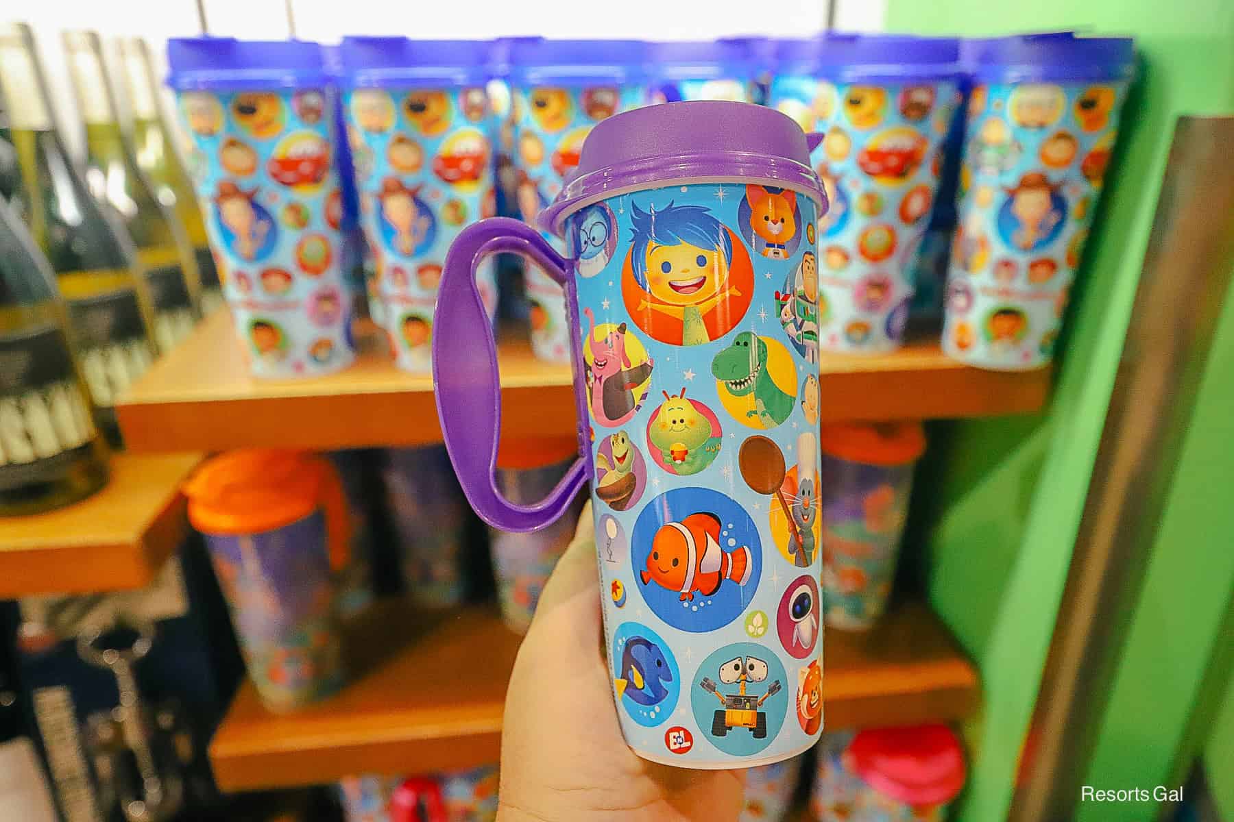 a hand holding a purple mug with Pixar characters 