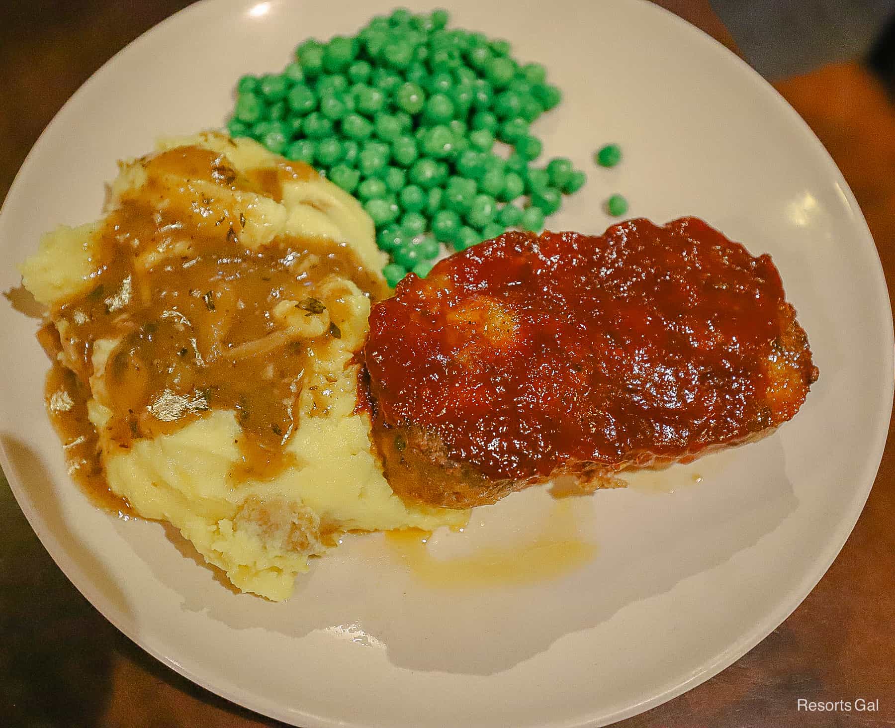 a platter of meatloaf topped with sauce, mashed potatoes and gravy and green peas 