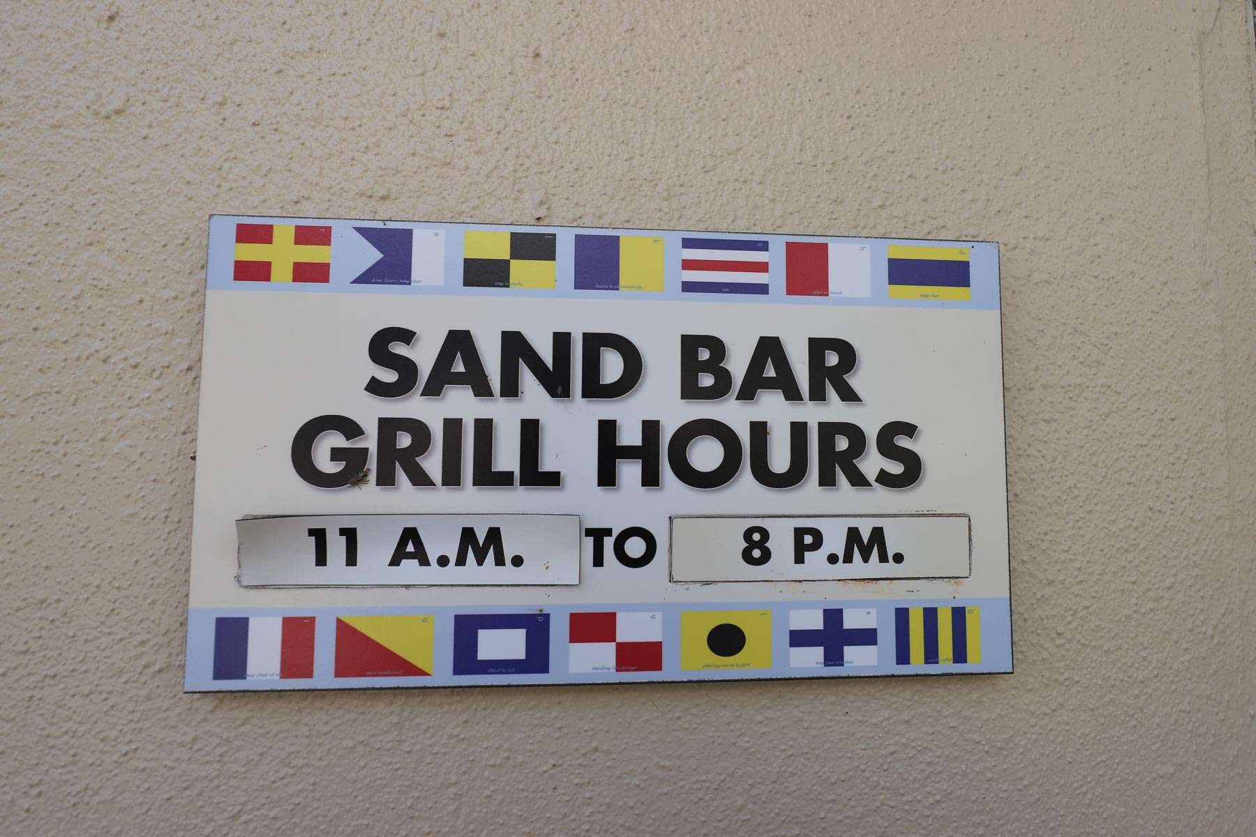 a sign with the posted hours for the Sand Bar 