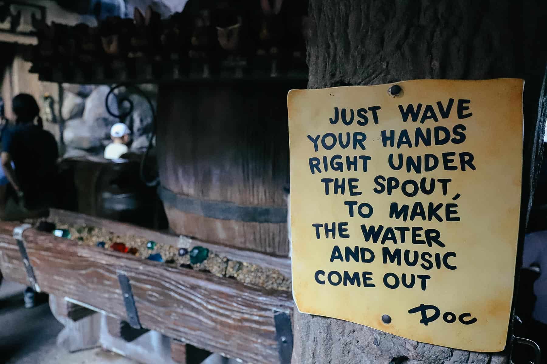 An interactive queue element sign that reads "Just wave your hands right under the spout, to make the water and music come out." 