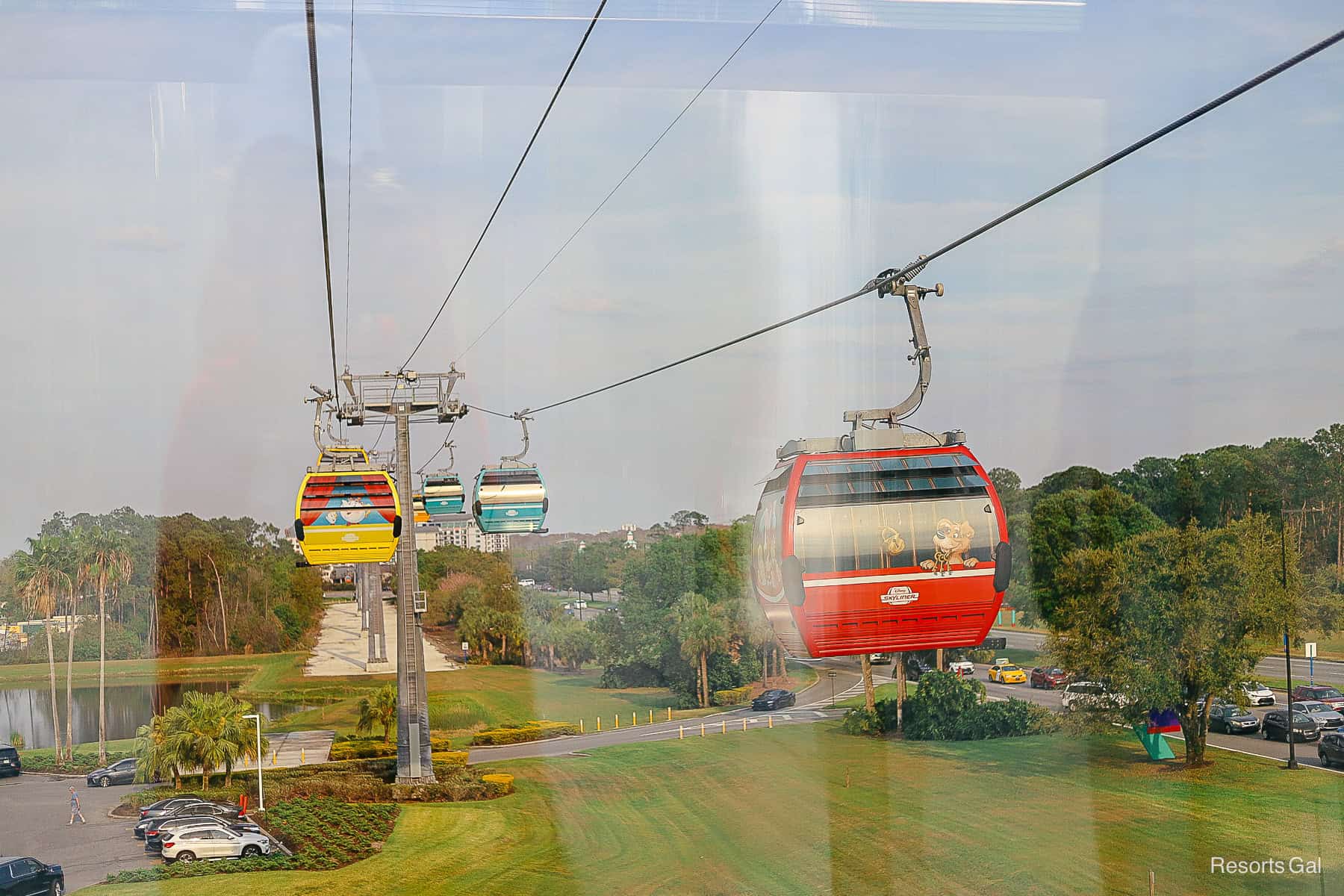 Skyliner gondolas travel past cars sitting in traffic underneath them.