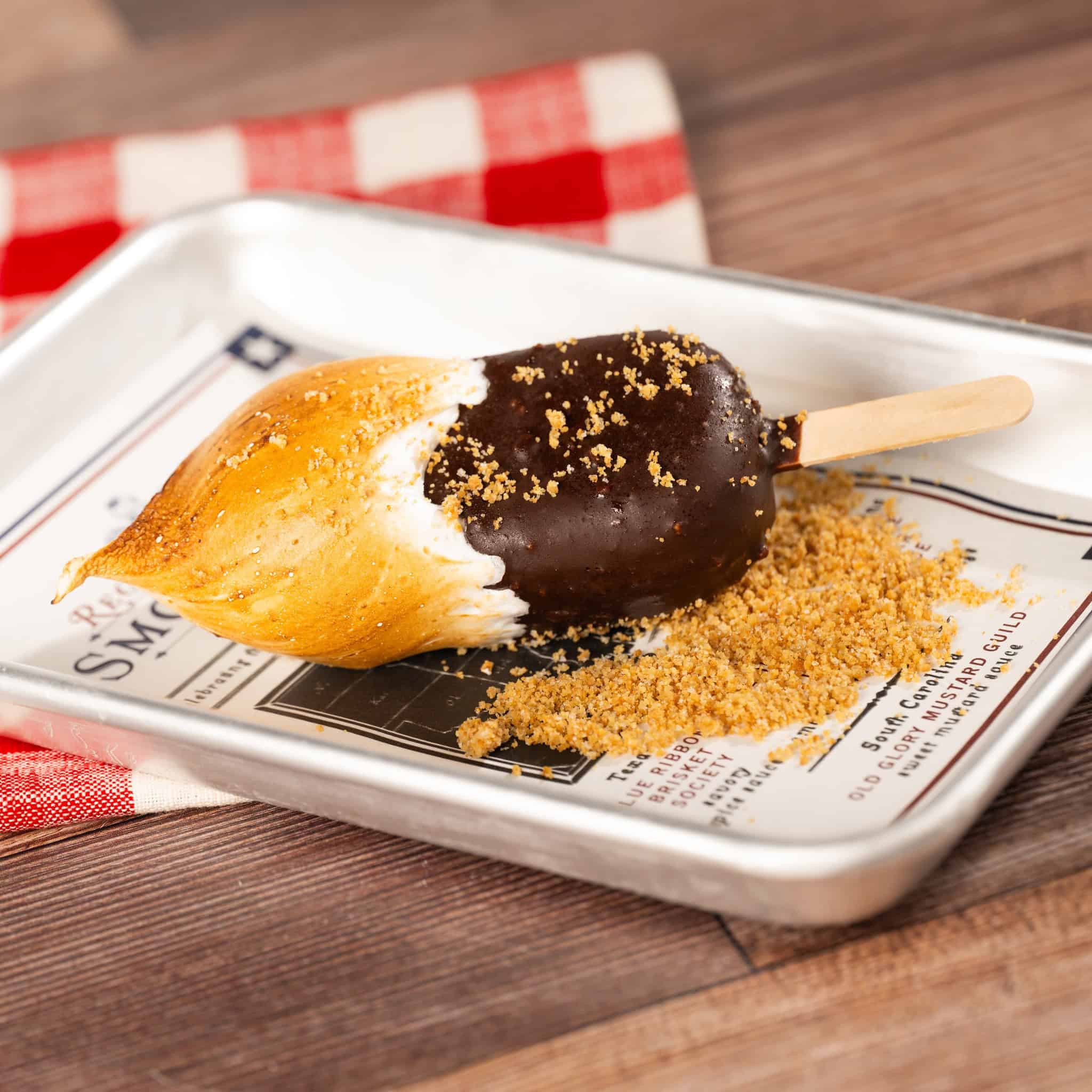 a popsicle that's chocolate with a white topped and caramelization like it's been roasted surrounded by graham cracker crumbs 