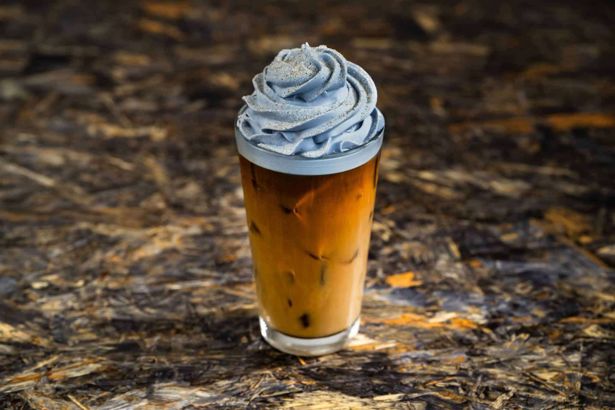 a tall glass of a coffee drink with light grey whipped topping