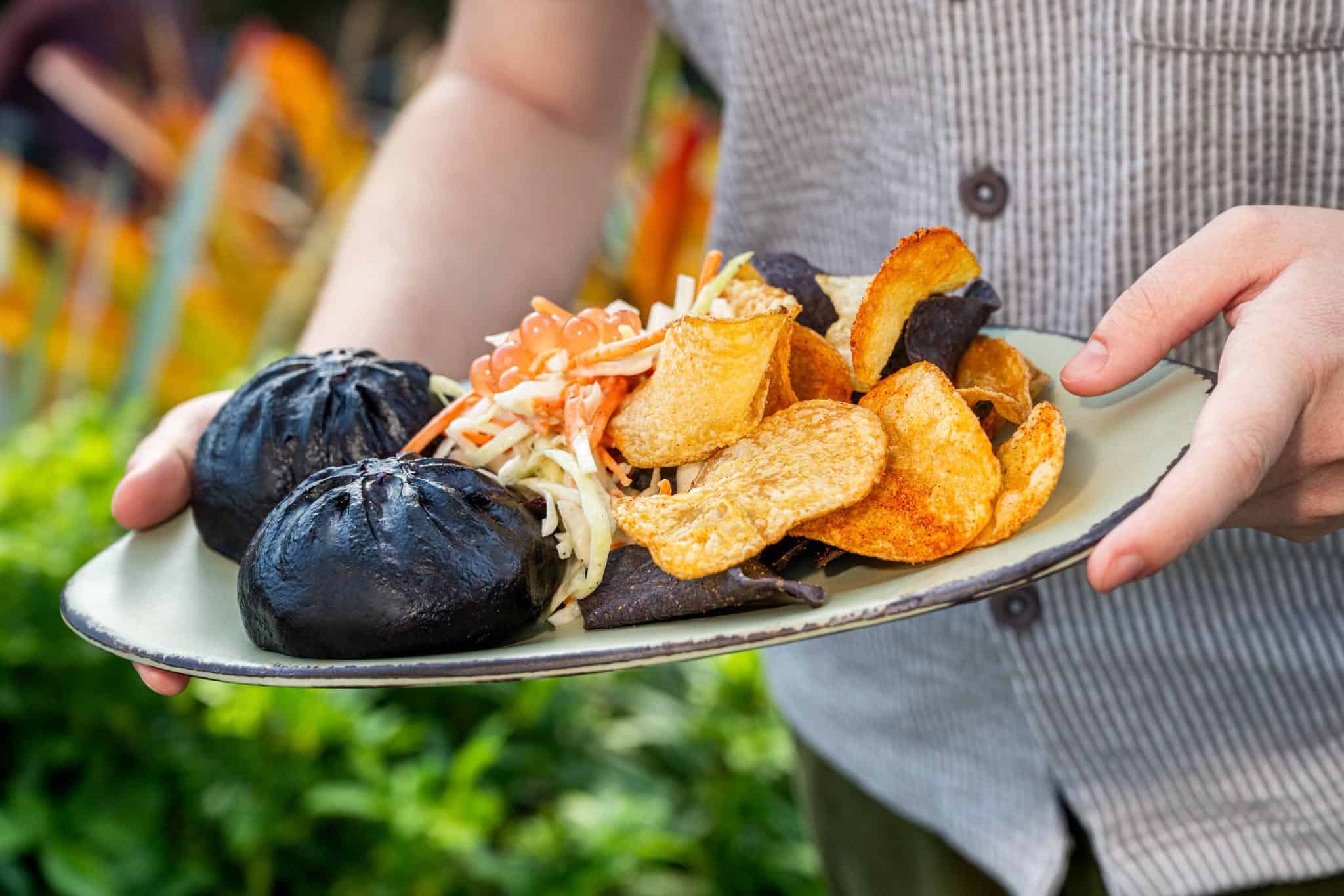 a hand holding a plate of spicy pork pods with eggplant color and chips