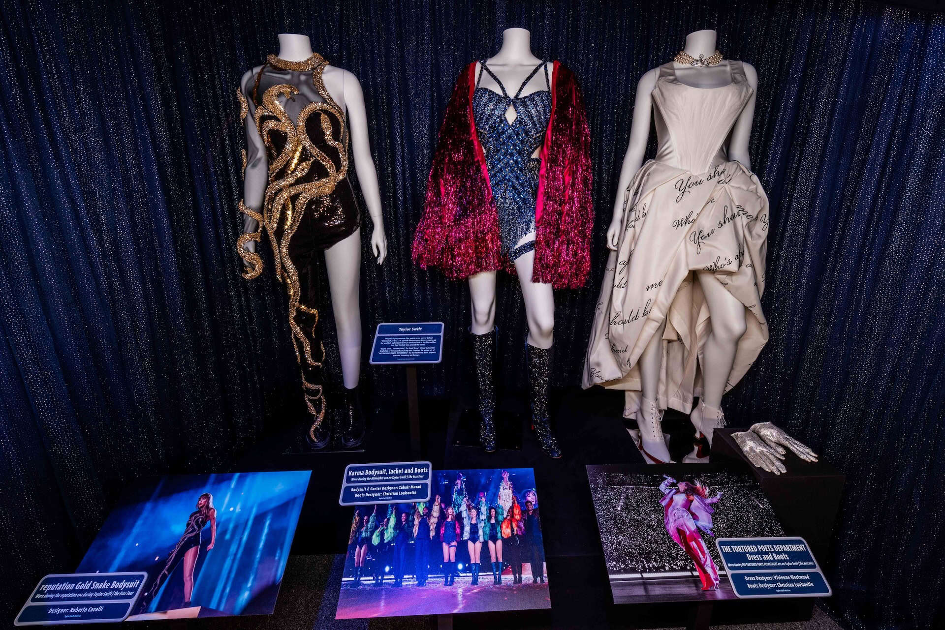 three dresses from "reputation", “THE TORTURED POETS DEPARTMENT,” and “Midnights” eras in a case at Walt Disney Presents