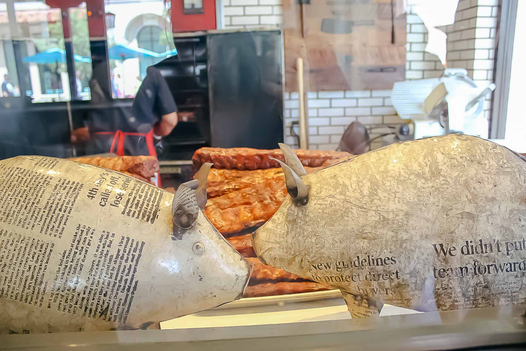 Two decorative pigs in front of slabs of pork inside The Polite Pig. 