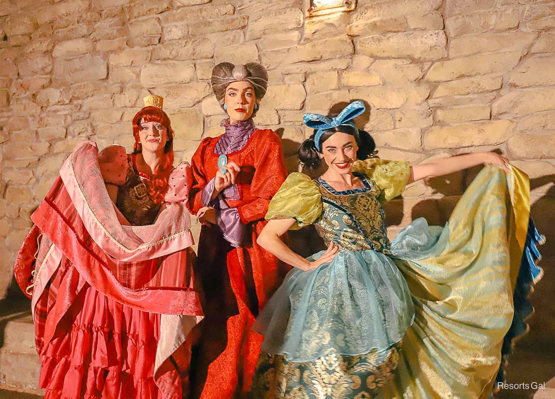 Anastasia and Drizella pose with dresses on display. Lady Tremaine stands in the center.